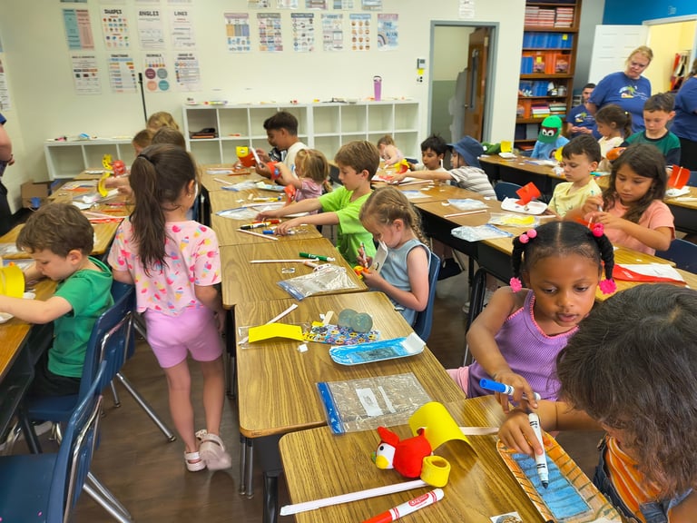 Elementary school children working on art and craft projects at tables in a colorful classroom.