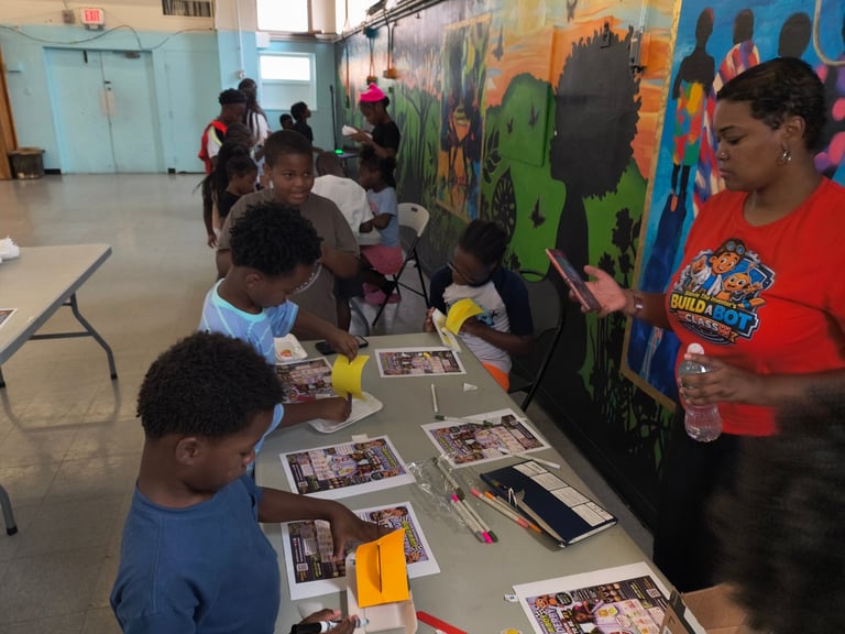 Children participate in an art activity at a table with magazines and materials, while colorful murals are visible in an indoor community space.