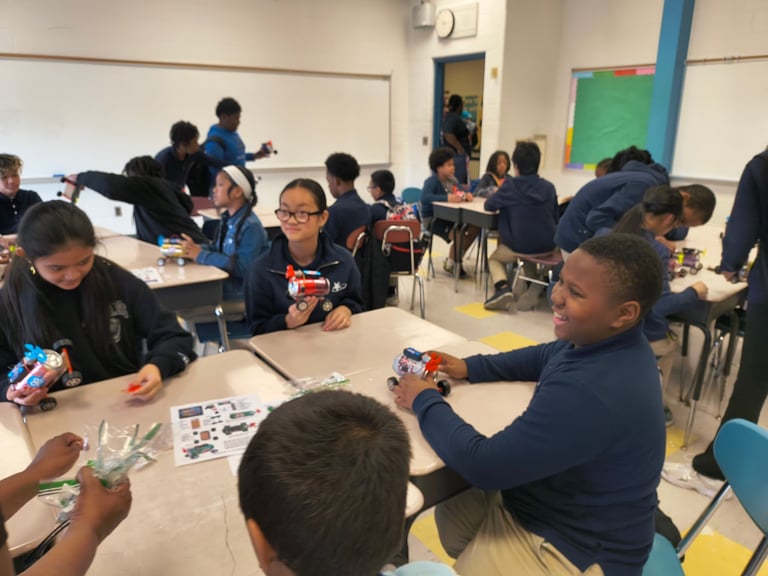 Classroom full of students in dark blue uniforms participating in a hands-on activity or workshop at tables.