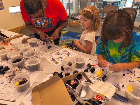 Three children engaged in a colorful hands-on activity with materials spread across a table.
