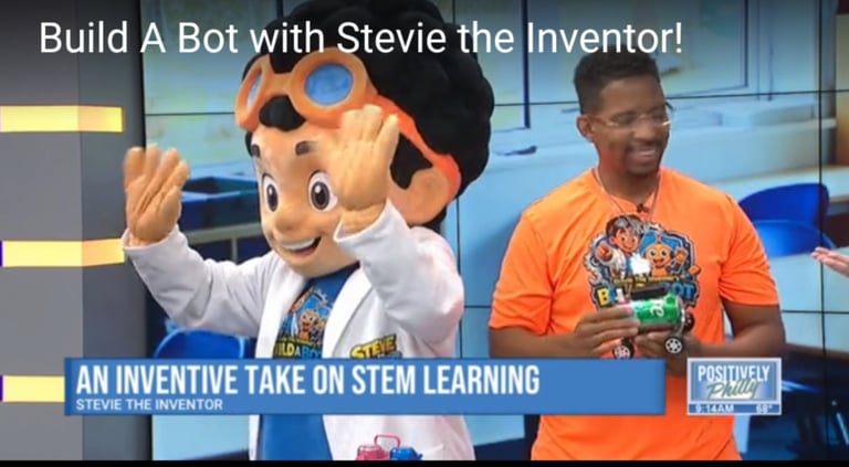 Stevie the Inventor mascot in white lab coat waves next to a man in orange shirt holding a robot, promoting STEM learning